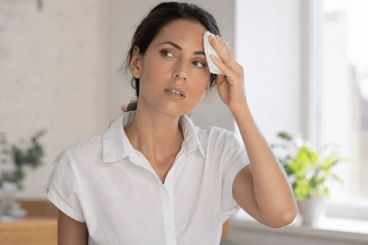 Femeie adultă ștergându-și fruntea cu un prosop mic într-o cameră răcoroasă de vară