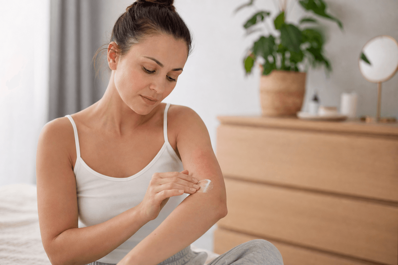 Femeie adultă îngrijind o zonă de piele uscată și iritată într-un cadru editorial natural