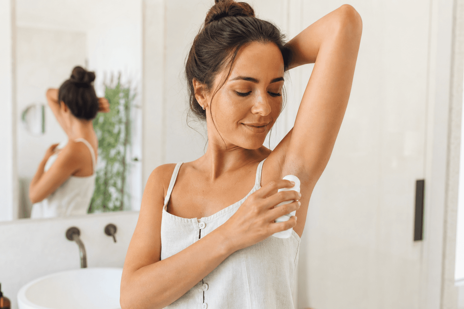 Femeie adultă aplicând deodorant într-o baie luminoasă, într-o rutină simplă de vară